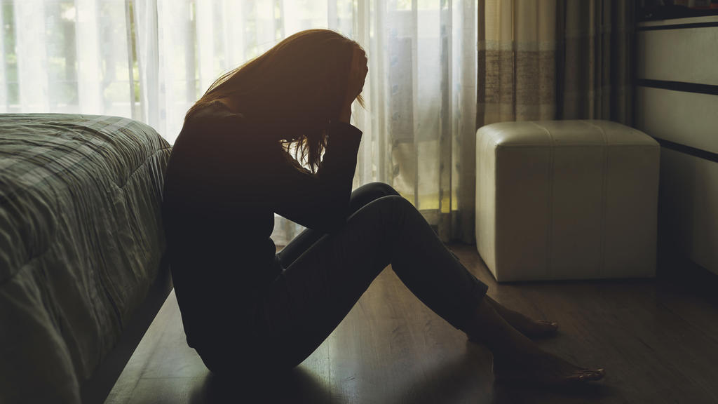depressed woman sitting head in hands in the dark bedroom