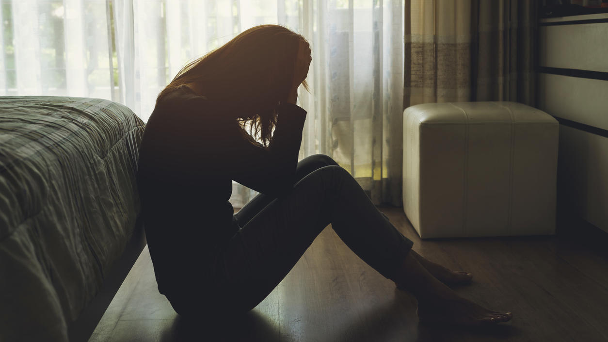 Eine depressive Frau sitzt am Boden ihres Schlafzimmers