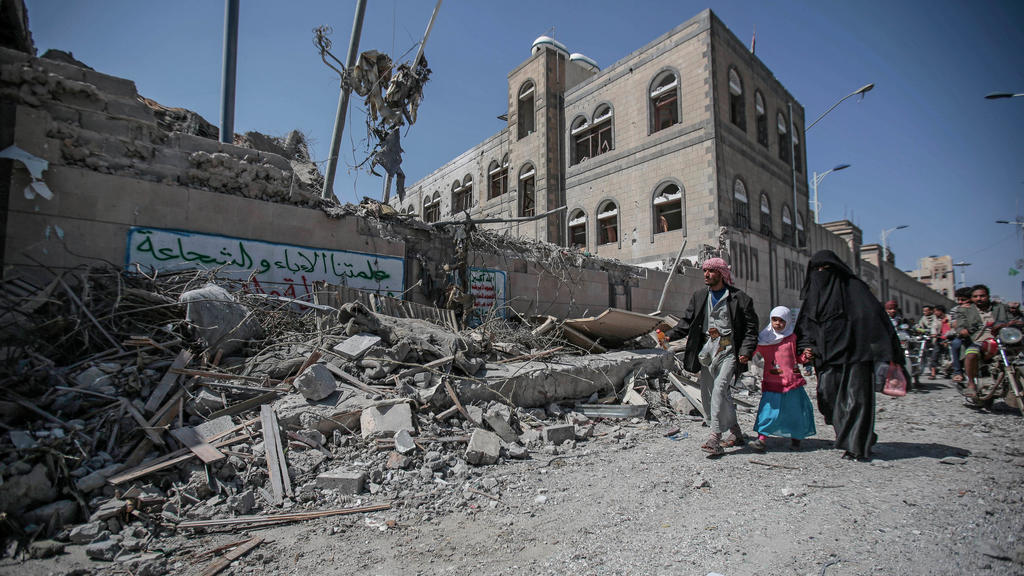 07.05.2018, Jemen, Sanaa:Eine Familie aus dem Jemen geht an Trümmern, die zu einem Präsidentenkomplex gehörten und bei einem Luftangriff getroffen wurden, vorbei. Nach Angaben der Regierung sind bei einem Luftangriff auf Sanaa mindestens sechs Mensch