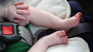 Legs and hand of little child in car seat.