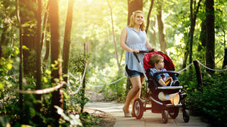 Strahlende Mutter macht mit ihrem Baby im Kinderwagen einen Spaziergang durch den Wald