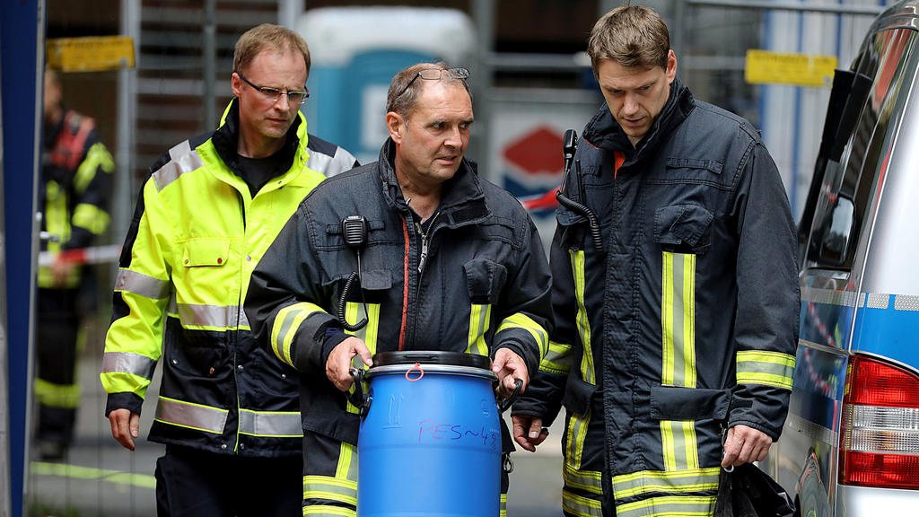 15.06.2018, Nordrhein-Westfalen, Köln: Ein Feuerwehrmann trägt vor dem Wohnkomplex Osloerstr. 3 in Köln-Chorweiler eine Tonne raus. Nach dem Fund von hochgiftigem Rizin in einem Hochhaus in Köln will die Polizei am Freitagmorgen mehrere leerstehende