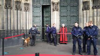 22.06.2018, Nordrhein-Westfalen, Köln: Ein Polizist mit einem Spürhund geht in den gesperrten Dom. Die Kirche ist wegen eines verdächtigen Mannes evakuiert worden. Der Mann habe sich auffällig verhalten und sei daraufhin von Polizisten in Gewahrsam genommen worden, sagte eine Polizeisprecherin am Freitag. Foto: Katharina Hensel/dpa +++ dpa-Bildfunk +++