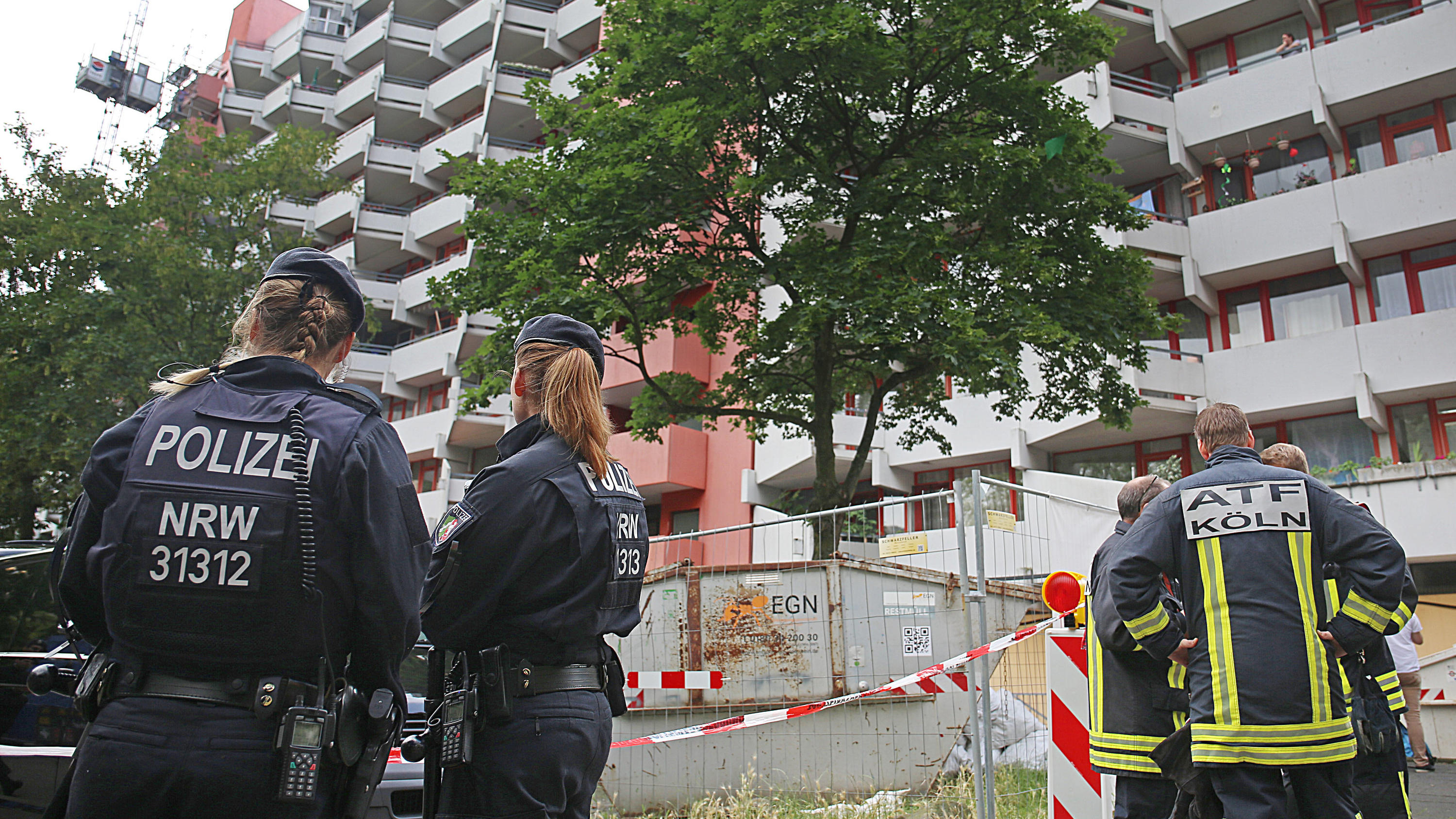 15.06.2018, Nordrhein-Westfalen, Köln: Polizisten und Feuerwehrleute stehen vor dem Wohnkomplex Osloerstr. 3 in Köln-Chorweiler. Nach dem Fund von hochgiftigem Rizin in einem Hochhaus in Köln will die Polizei am Freitagmorgen mehrere leerstehende Woh