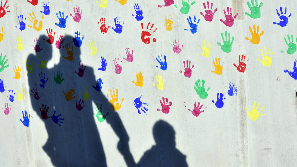 SYMBOLBILD - 08.04.2015, Bayern, München: Ein Mann mit einem Kind auf dem Arm und einem an der Hand wirft einen Schatten auf eine mit bunten Handabdrücken bemalte Wand einer Kindertagesstätte. (zu dpa ««Keine Sieger, keine Verlierer» - 1,6 Milliarden