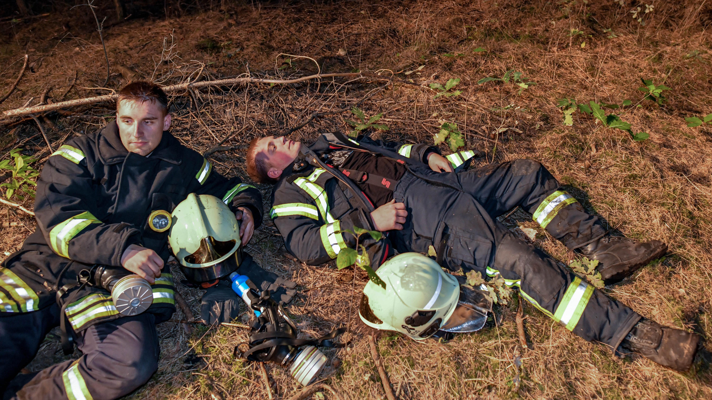 24.08.2018, Brandenburg, Klausdorf: Zwei erschöpfte Kameraden der Freiwilligen Feuerwehr ruhen sich nach ihrem Einsatz aus. Ein Feuer hat sich im Südwesten Brandenburgs auf einer großen Waldfläche ausgebreitet. Rund 300 Einsatzkräfte bekämpfen den Wa