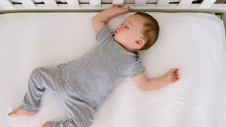 Baby schläft auf Matratze im Babybett