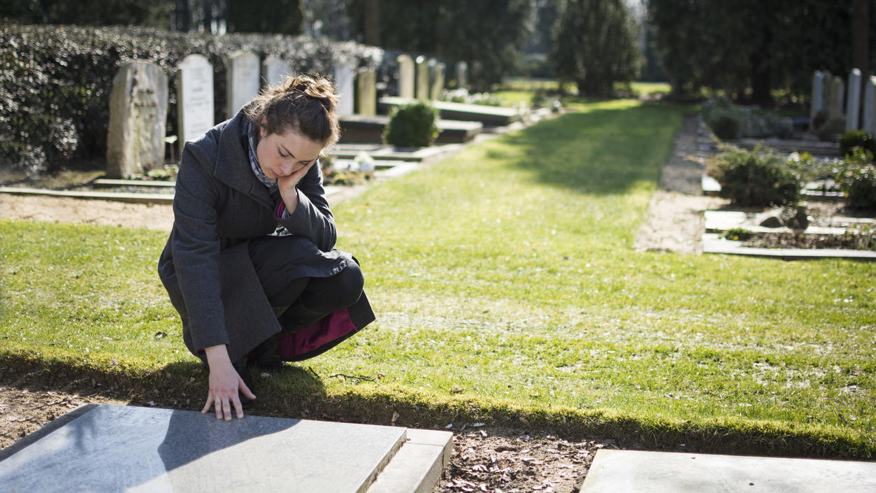 Eine trauernde Frau vor einem Grabstein auf dem Friedhof