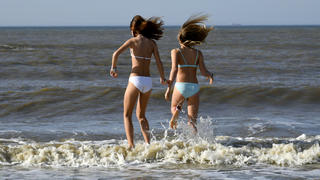 13.10.2018, Niederlande, Bloemendaal An Zee: Zwei Mädchen springen bei sonnigem Wetter am Strand über Wellen der Nordsee. Foto: Ina Fassbender/dpa +++ dpa-Bildfunk +++