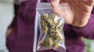 Ein Mann hält ein Tütchen mit Marihuana in die Kamera.