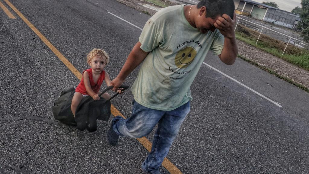 21.10.2018, Mexiko, Ciudad Hidalgo: Ein mittelamerikanischer Migrant marschiert mit seinem Kind Richtung USA. Die Migranten aus Honduras, El Salvador und Guatemala haben den Grenzzaun zwischen Guatemala und Mexiko überwunden, um von dort aus bis an d