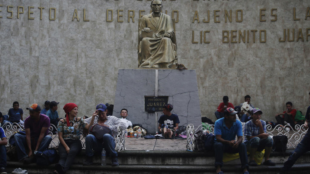 21.10.2018, Mexiko, Tapachula: Migranten aus Mittelamerika sitzen um eine Statue des ehemaligen mexikanischen Präsidenten Benito Juarez. Migranten aus Honduras, El Salvador und Guatemala haben den Grenzzaun zwischen Guatemala und Mexiko überwunden, u
