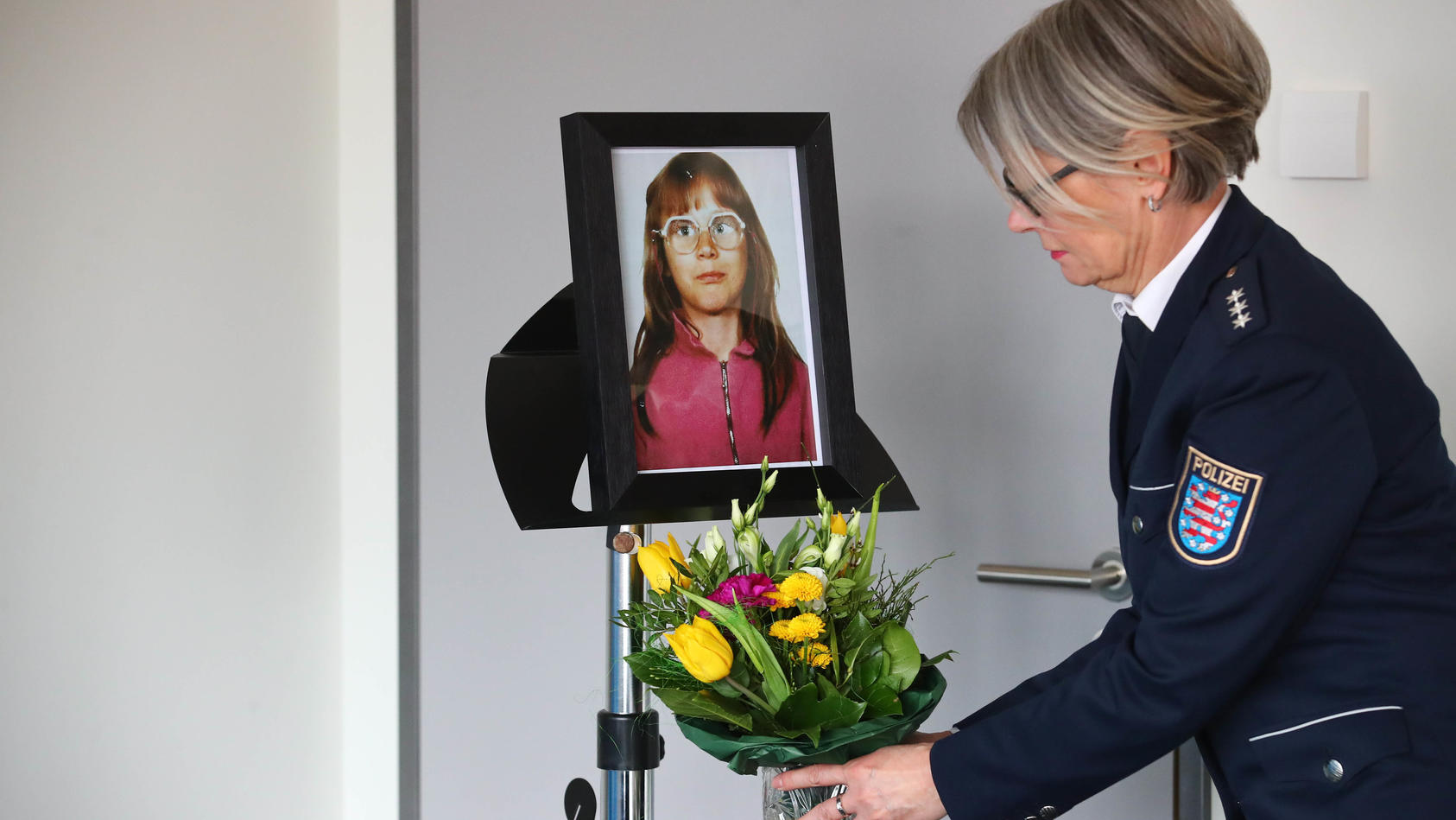 ARCHIV - 06.03.2018, Thüringen, Jena: Eine Beamtin der Polizei Jena stellt vor einer Pressekonferenz einen Blumenstrauß unter das Foto der ermordeten Stephanie. Im Fall aus dem Jahre 1991 war ein tatverdächtiger Mann festgenommen worden. Der Fall ist