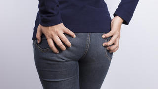 Eine Frau in Jeans hält die Hände an ihrem Gesäß.