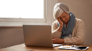 Romance Scam: Eine ältere Frau sitzt besorgt an ihrem Laptop.