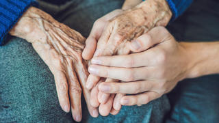 Eine jüngere Hand liegt auf der Hand einer älteren Person.