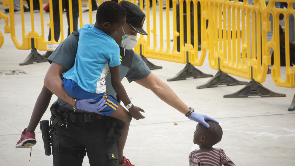 ARCHIV - 01.08.2018, Spanien, Los Barrios: Ein Beamter der Guardia Civil trägt ein Flüchtlingskind in einem Sportzentrum in Los Barrios, Südspanien, nachdem ed am Mittwoch, dem 1. August 2018, vom spanischen Rettungsdienst in der Straße von Gibraltar