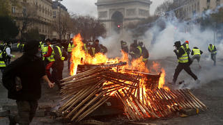 01.12.2018, Frankreich, Paris: Demonstranten laufen an einer brennenden Barrikade in der Nähe des Arc de Triomphe (Triumphbogen) während einer Demonstration vorbei. Mehrere Hundert Demonstranten in gelben Westen haben sich am Samstagmorgen rund um die Pariser Prachtstraße Champs-Elysees versammelt. Foto: Thibault Camus/AP/dpa +++ dpa-Bildfunk +++