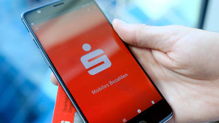 ILLUSTRATION - 30.07.2018, Berlin: Ein Mann hält eine EC-Karte und ein Mobiltelefon, auf dem der Startbildschirm der Mobiles Bezahlen - App der Sparkasse dargestellt wird, in der Hand. Mit dem Smartphone statt Bankkarte an der Ladenkasse zahlen können inzwischen - zumindest technisch gesehen - viele in Deutschland. Foto: Fabian Sommer/dpa +++ dpa-Bildfunk +++