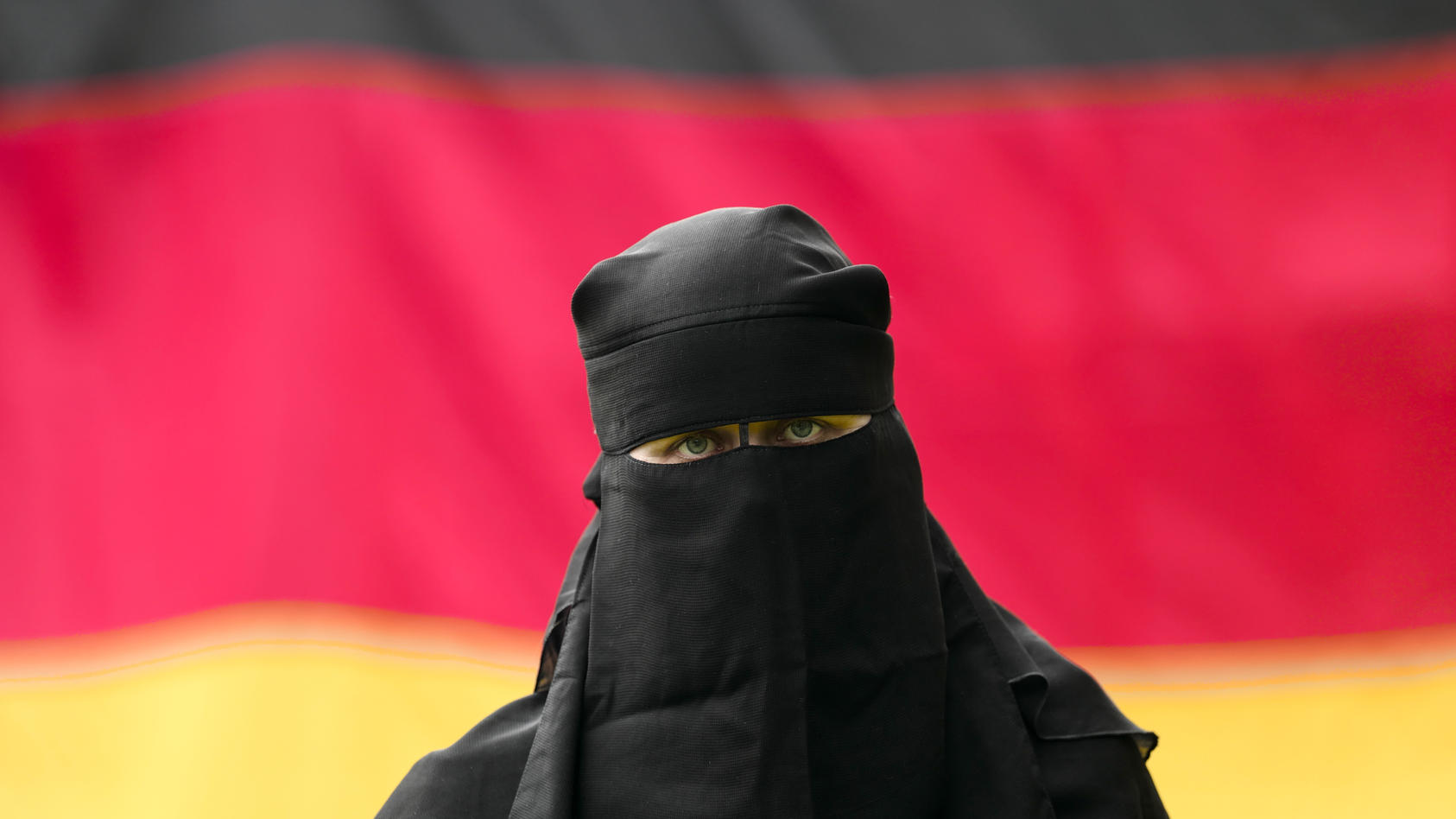 ILLUSTRATION - Eine Frau trägt einen Nikab vor einer Deutschlandfahne am 26.08.2017 in Leipzig (Sachsen, gestellte Szene). Der Nikab ist ein Gesichtsschleier, der von  muslimischen Frauen getragen wird. Fundamentalistische Moslems fordern bei ihrer A
