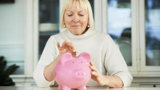 Eine Frau wirft Geld in ein Sparschwein.