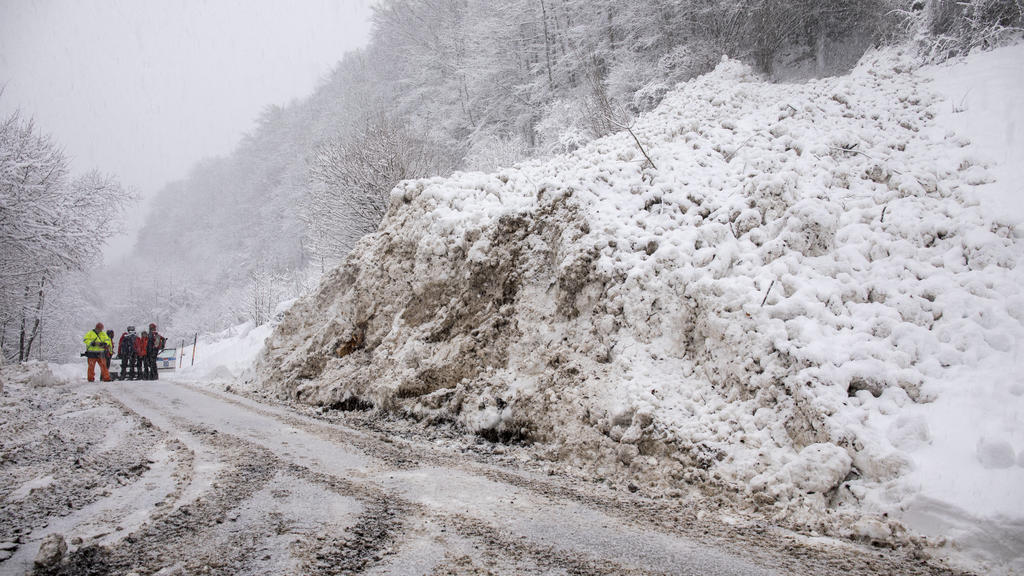 Einsatzkräfte räumen nach einer Lawine eine Straße frei.