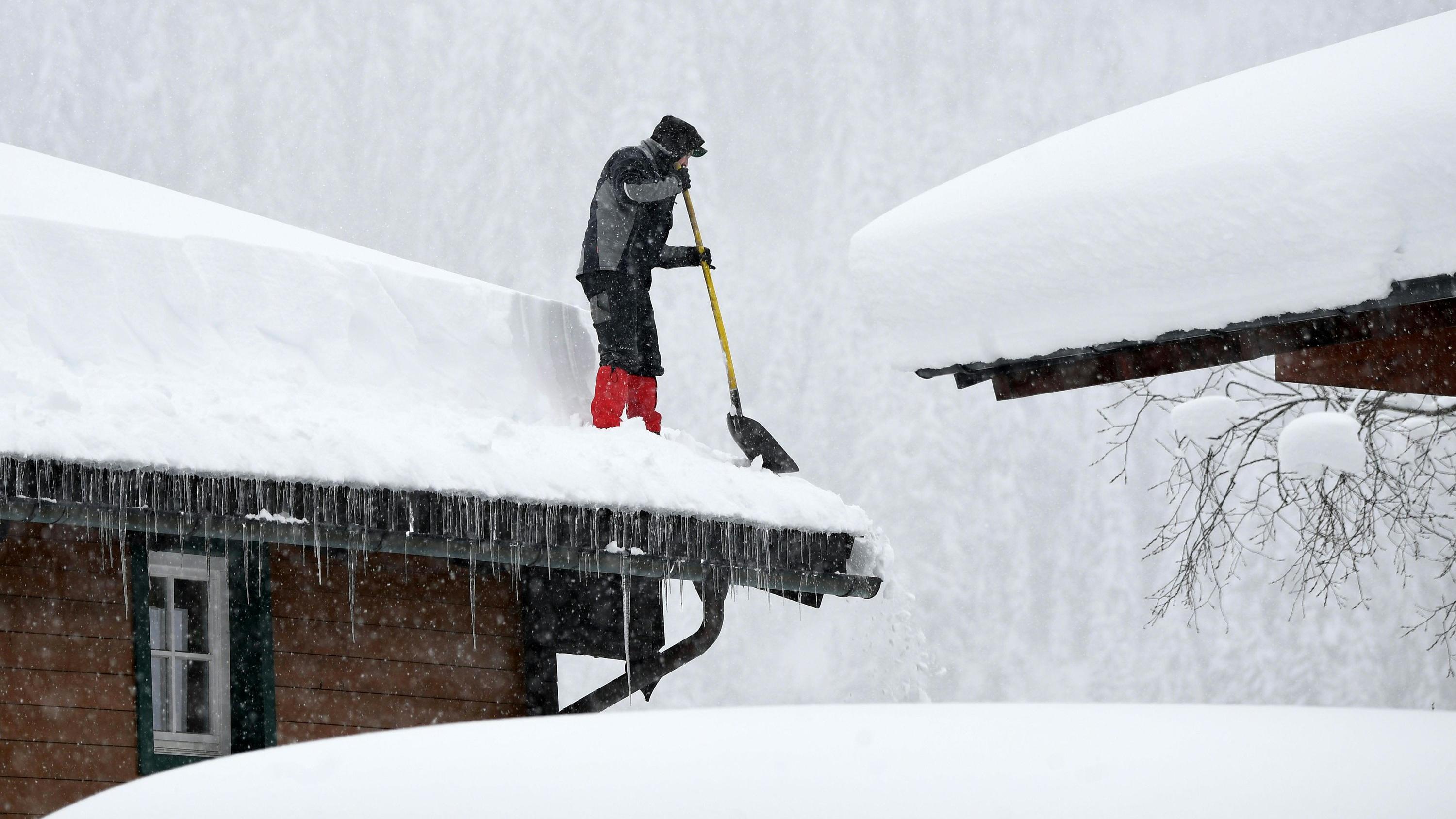 Ein Mann befreit ein Dach von der Schneelast. 