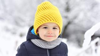 Cheerful kid smiling in winter snow park. Portrait of happy joyful beautiful little boy on white background of snowing trees. Happy childhood on walk, child smile to camera. Beautiful child portrait