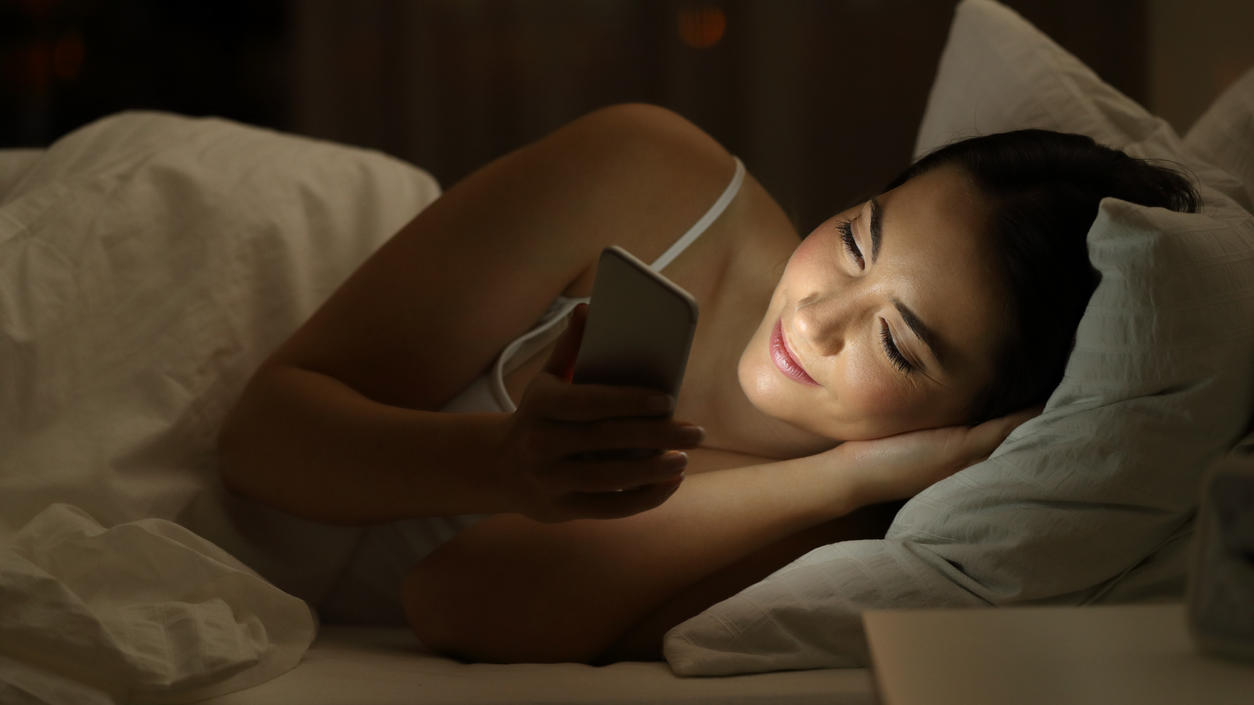 Junge Frau liegt mit Smartphone im Bett