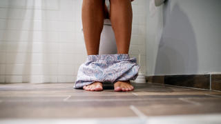 Beine und Höschen einer Frau, die auf der Toilette sitzt