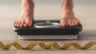 Cropped image of woman feet standing on weigh scales, on gray background. A tape measure in the foreground
Frau steht auf Waage, vor ihr liegt ein Maßband