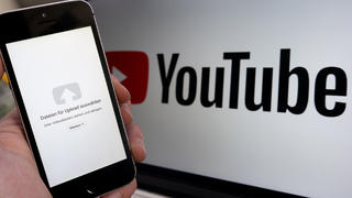 ILLUSTRATION - 14.02.2019, Niedersachsen, Hannover: - ARCHIV - Ein Upload-Fenster der Video-Plattform Youtube ist auf einem Smartphone vor einem YouTube-Logo auf einem Bildschirm zu sehen. (zu dpa: «Europaweiter Protest gegen neues Urheberrecht und Artikel 13») Foto: Raphael Knipping/dpa +++ dpa-Bildfunk +++