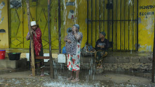 28.04.2019, Mosambik, Pemba: Drei Frauen warten vor einem geschlossenen Laden während es in Strömen regnet. Mosambik kämpft mit den Folgen von Zyklon «Kenneth». Schwere Regenfälle haben nach Angaben von Helfern im Norden des Landes Überschwemmungen verursacht. Bislang seien infolge des Wirbelsturms acht Menschen in Mosambik und auf dem Inselstaat der Komoren gestorben. Tausende Häuser seien zerstört. Foto: Tsvangirayi Mukwazhi/AP/dpa +++ dpa-Bildfunk +++
