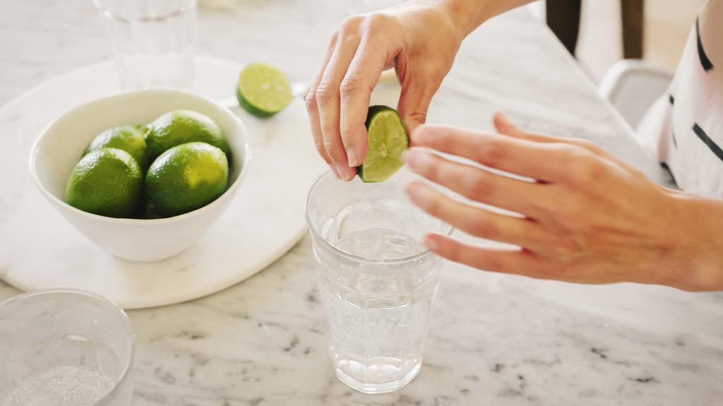 A woman squeezing fresh limes into a glass of water. A woman squeezing fresh limes into a glass of water. PUBLICATIONxINxGERxSUIxAUTxHUNxONLY 22164