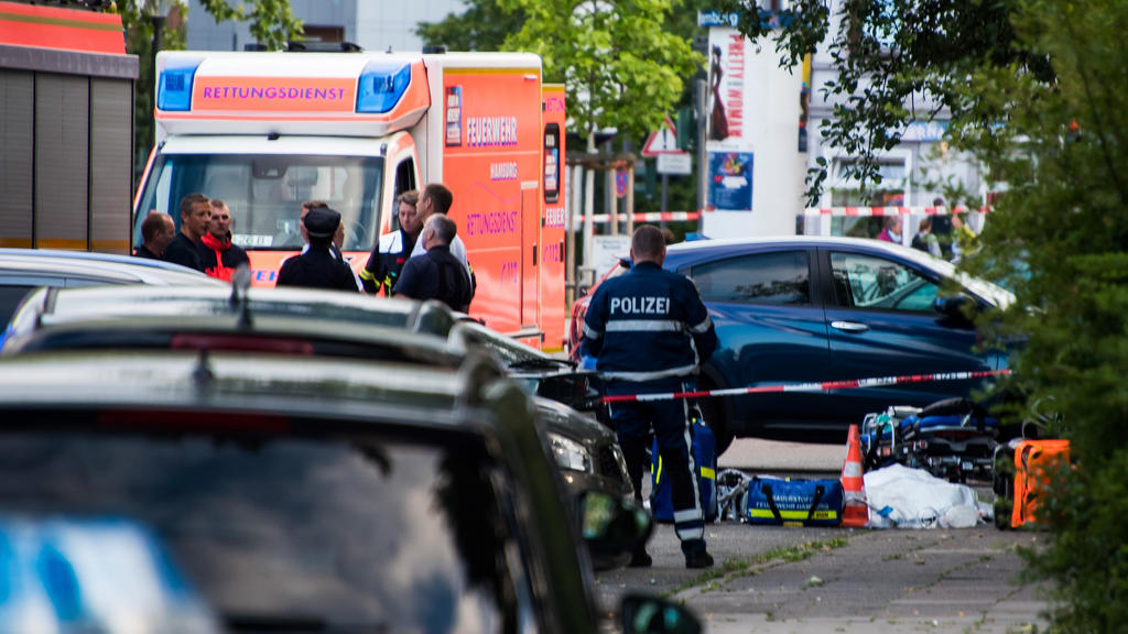 27.06.2019, Hamburg: Polizisten und Feuerwehrleute, stehen an einer abgesperrten Straße neben einem abgedeckten Körper. Ein Mann ist in Hamburg-Lohbrügge am erschossen worden. Einzelheiten oder Hintergründe konnte ein Sprecher des Lagezentrums der Po