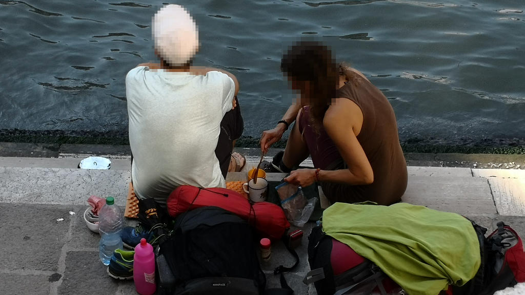 HANDOUT - 19.07.2019, Italien, Venedig: Zwei deutsche Touristen sitzen mit ihrem Gepäck an der Treppe der Rialto-Brücke und kochen sich mit einem kleinen Kaffeekocher einen Kaffee auf dem Gehweg. (zu dpa "Deutsche Touristen kochen Kaffee in Venedig -