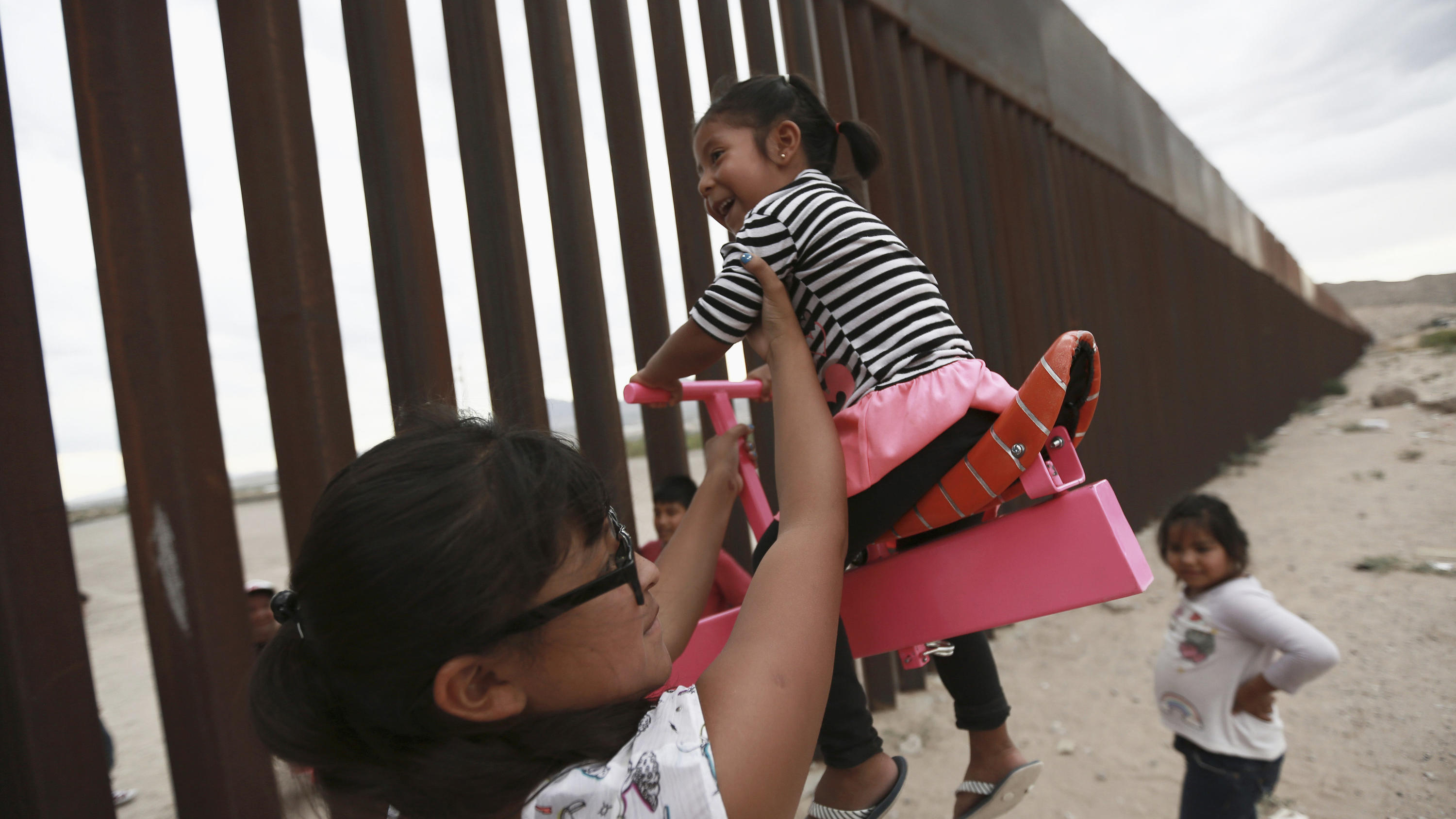 28.07.2019, Mexiko, Ciudad Juarez: Eine Frau spielt mit Mädchen an einer Wippe, die am Grenzzaun zwischen Mexiko und den USA angebracht ist. Die Wippe wurde von Ronald Rael, einem Professor für Architektur in Kalifornien, entworfen. Foto: Christian C