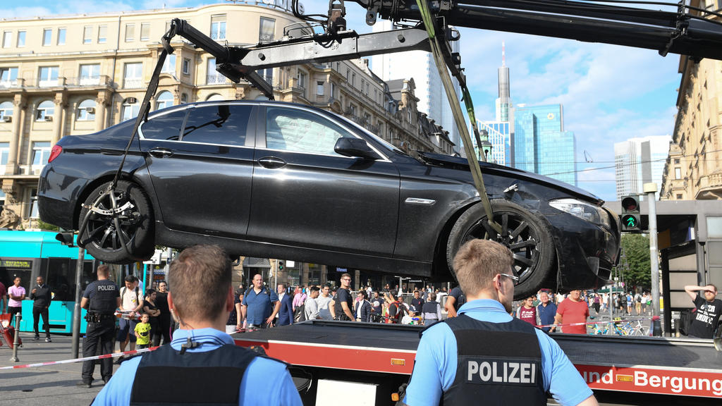 02.08.2019, Hessen, Frankfurt/Main: Polizeibeamte stehen am Frankfurter Hauptbahnhof vor einem Fahrzeug, das zur polizeilichen Untersuchung abgeschleppt wird. Mehrere Täter waren nach einem Banküberfall mit dem schwarzen BMW geflüchtet. Wegen des Pol