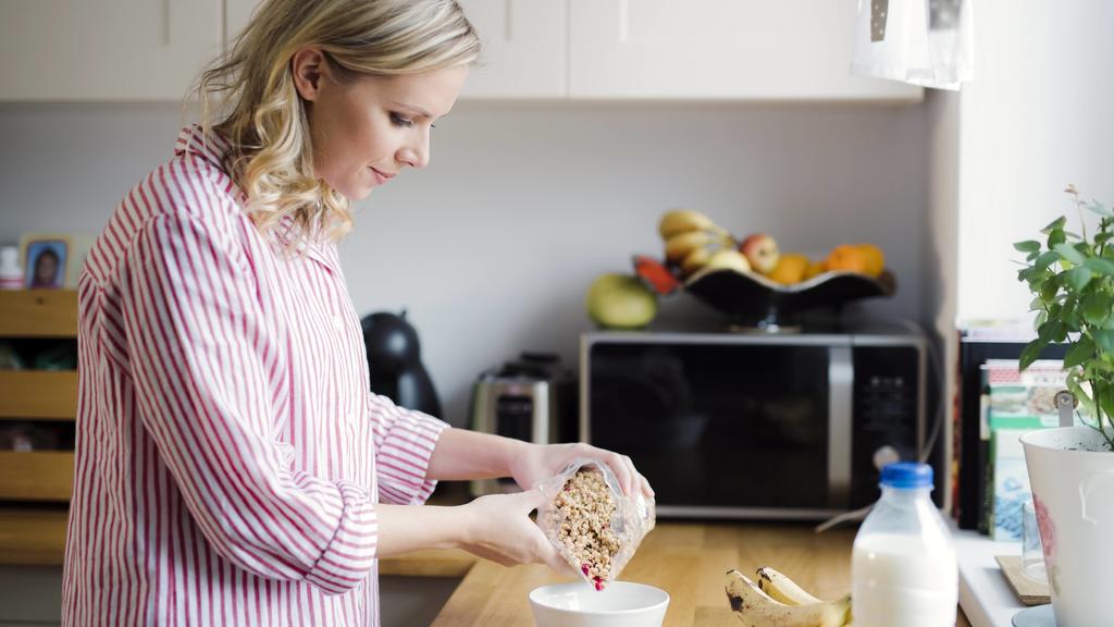 Eine Frau bereitet sich in der Küche ein gesundes Frühstück, bestehend aus Müsli und Joghurt, zu.