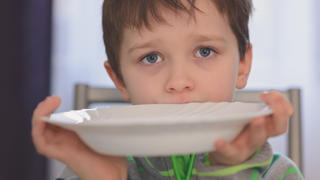 Kind sitzt vor einem leeren Teller
