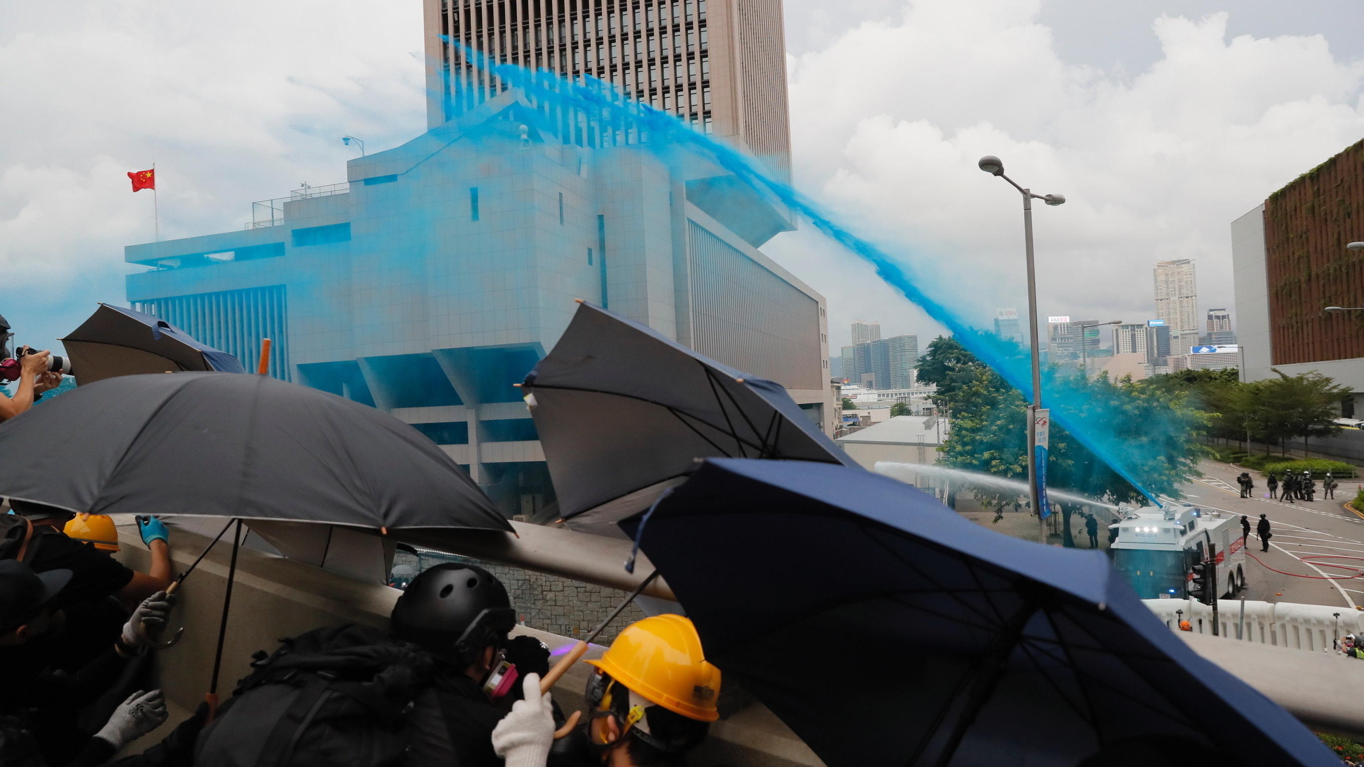 31.08.2019, China, Hongkong: Demonstranten schützen sich mit Regenschirmen vor der Polizei, die mit Wasserwerfern gegen sie vorgeht und die Demonstranten mit blauer Farbe besprüht. Trotz des Verbots einer Großdemonstration kommt es in Hongkong erneut