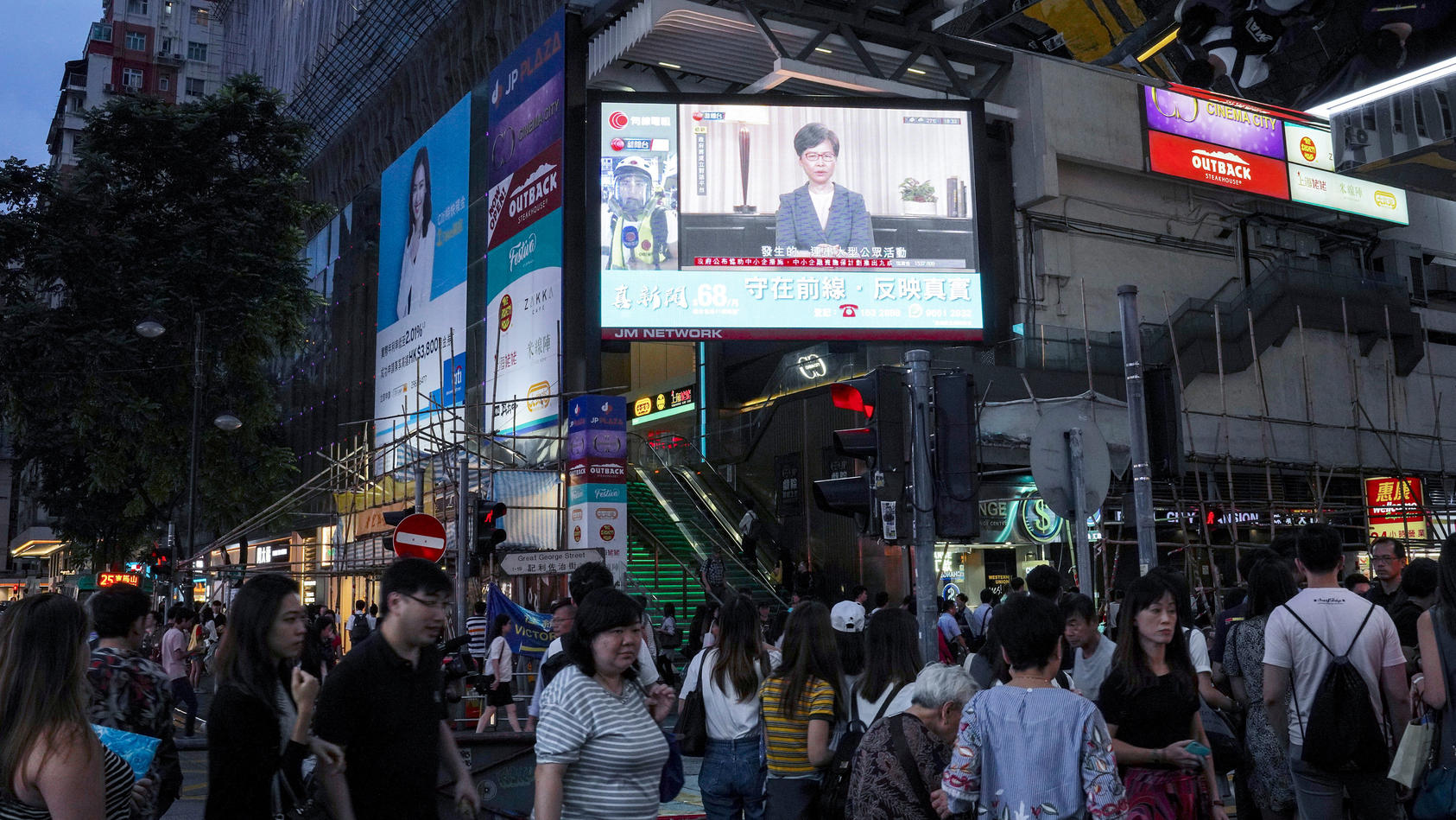 04.09.2019, China, Hongkong: Passanten gehen in der Innenstadt unter einem Bildschirm, auf dem Carrie Lam, Regierungschefin der chinesischen Sonderverwaltungszone Hongkong, bei einer Pressemitteilung zu sehen ist. Hongkongs Regierung hat den Entwurf 