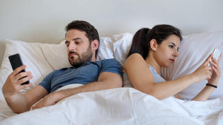 Paar mit Smartphones liegt lustlos im Bett