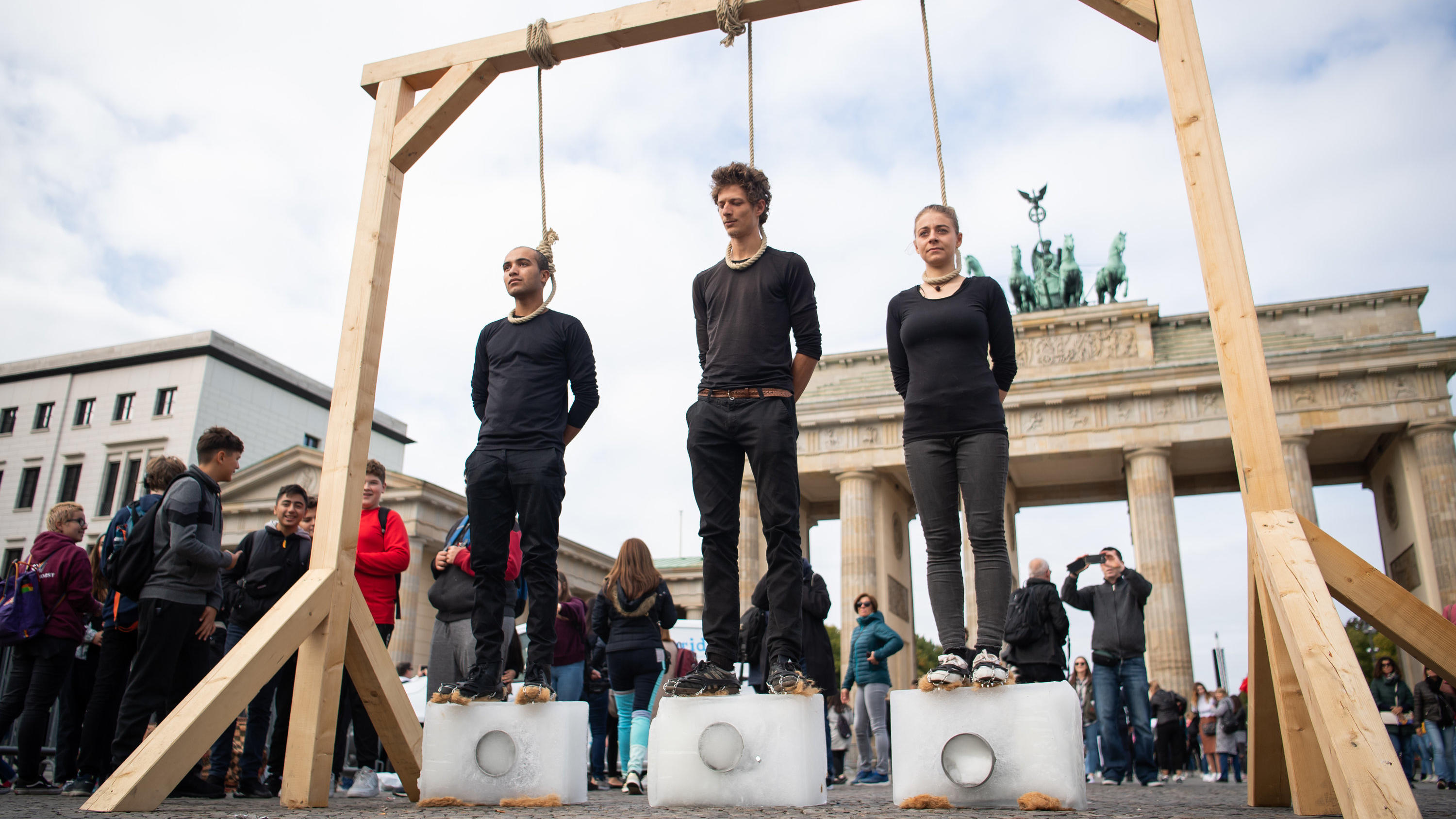 dpatopbilder - 20.09.2019, Berlin: Drei Demonstranten stehen unter einem Galgen mit einem Seil um den Hals auf Eisblöcken. Dahinter ist das Brandenburger Tor. Die Bewegung Fridays for Future hatte zum globalen Klimastreik aufgerufen. Foto: Tom Weller