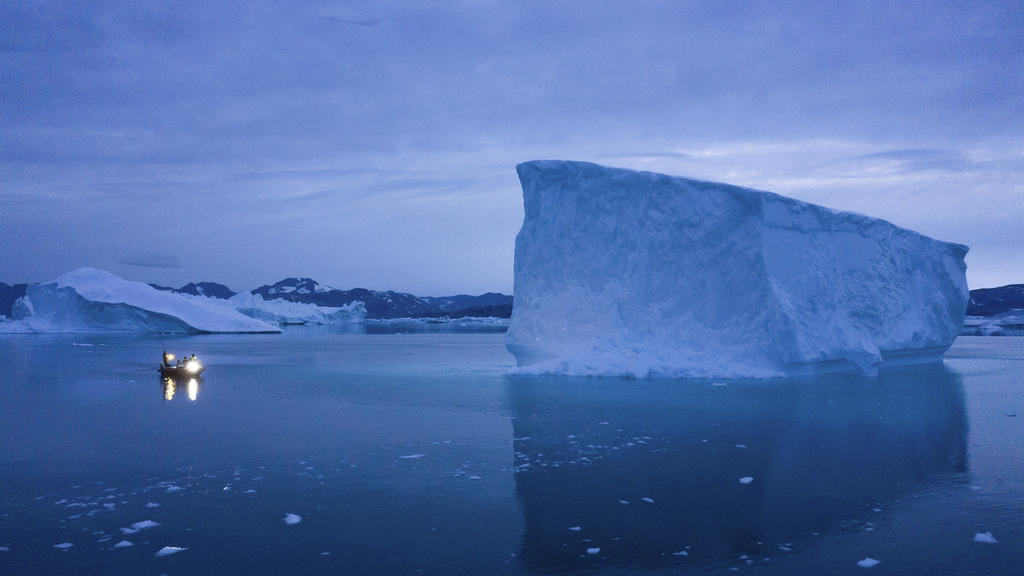 ARCHIV - 15.08.2019, Grönland, Kulusuk: Ein kleines Boot fährt an einem großen Eisberg in Ostgrönland vorbei. Mit der Erderwärmung dehnt sich das Meerwasser aus, die Eismassen schmelzen und der Meeresspiegel steigt. Den Einfluss von CO2 auf Meer und