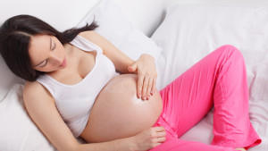 Pregnant woman putting a cream on a stomach at home