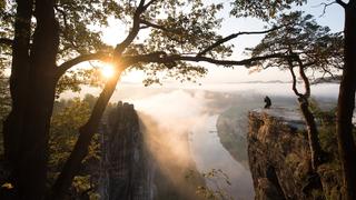 07.10.2019, Sachsen, Lohmen: Ein Mann hockt im Nationalpark Sächsische Schweiz auf dem Basteifelsen und fotografiert den Sonnenaufgang. Foto: Sebastian Kahnert/dpa-Zentralbild/dpa +++ dpa-Bildfunk +++