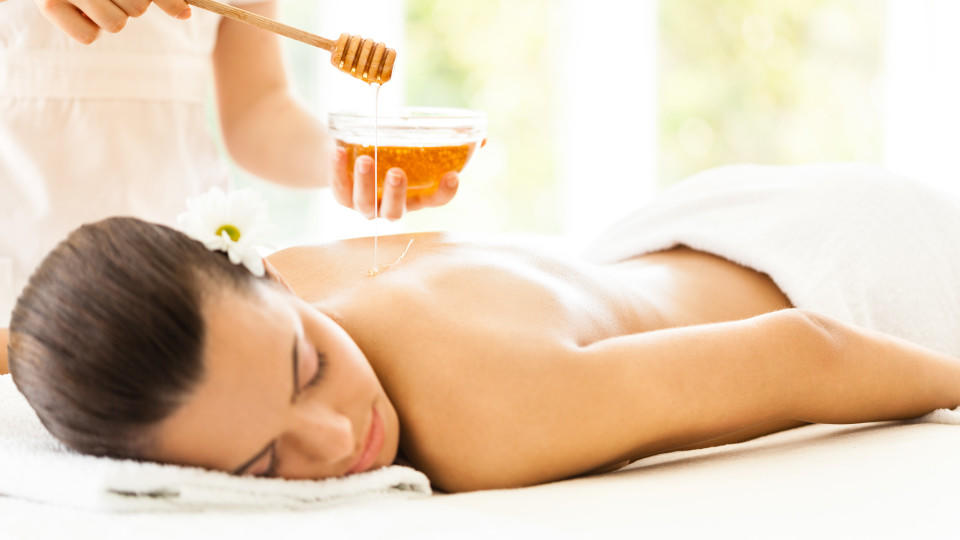 Masseuse pouring honey on woman's back