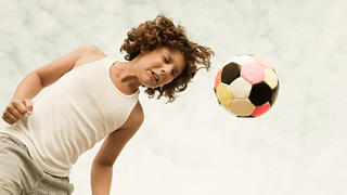 Kind köpft Ball beim Fußballspielen