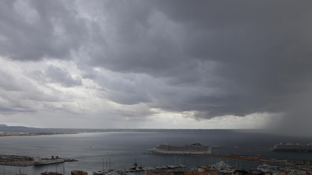 23.10.2019, Spanien, Palma de Mallorca: Dunkle Regenwolken hängen über der Bucht und dem Hafen, in dem zwei Kreuzfahrtschiffe liegen. Rund ums Mittelmeer haben heftige Unwetter vielerorts Überflutungen und Schäden verursacht. Foto: Clara Margais/dpa